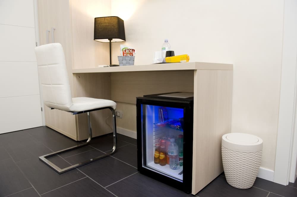 A cozy hotel room corner features a sleek desk with a modern chair, a lamp, and a mini-fridge stocked with drinks, ideal for travelers seeking comfort and convenience.