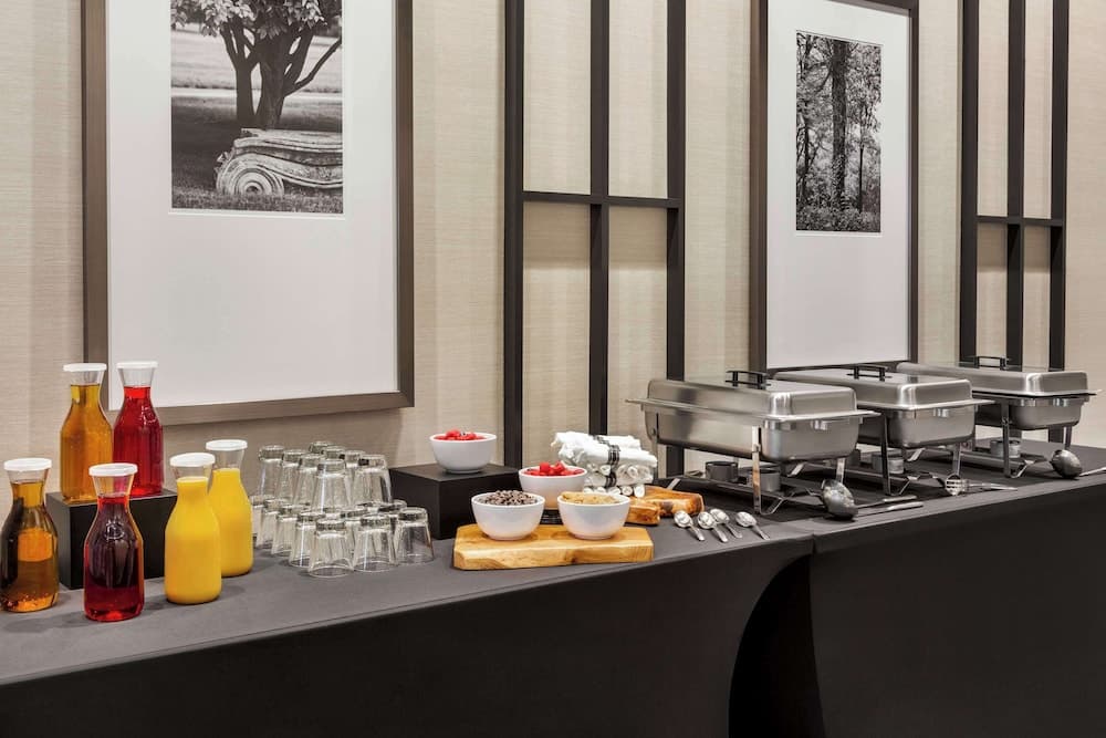A cozy hotel buffet setup features neatly arranged food trays, colorful beverages, and fresh fruit bowls against a backdrop of elegant wall art, ideal for travelers seeking a comfortable dining experience.