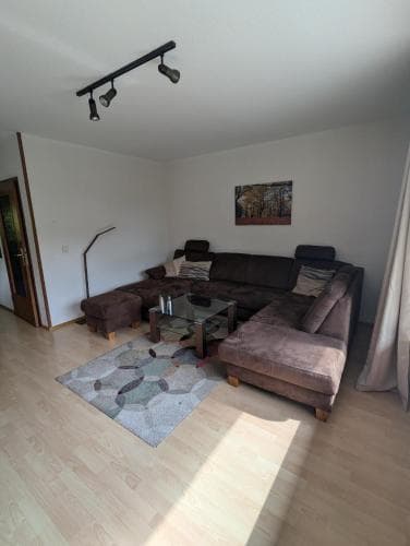 A cozy living room with a plush sectional sofa, modern track lighting, and a colorful rug creates a welcoming atmosphere ideal for travelers seeking a comfortable stay in an apartment rental.