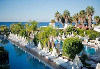A serene tropical resort features a long pool lined with white umbrellas and lounge chairs, surrounded by lush greenery and palm trees, ideal for a relaxing beach vacation getaway.