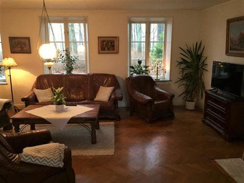 A cozy living room with leather furniture, warm lighting, and indoor plants creates an inviting atmosphere, perfect for travelers seeking a comfortable and homely accommodation.