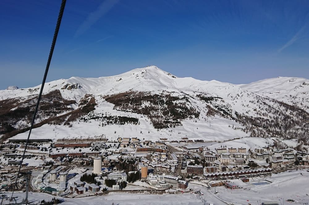 A breathtaking aerial view of a snowy mountain resort under a clear blue sky, showcasing ski slopes, dense forests, and modern buildings, ideal for winter sports enthusiasts seeking adventure and relaxation.