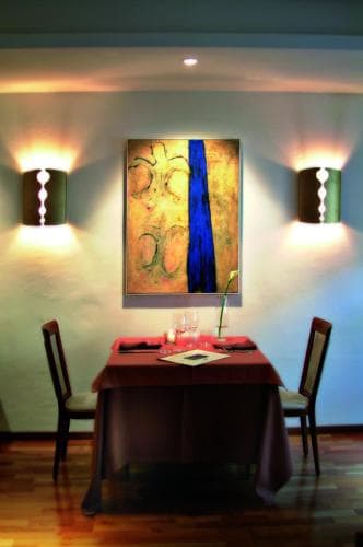 A cozy dining room with warm lighting, vibrant wall art, and a neatly set table creates an inviting atmosphere ideal for intimate gatherings or romantic dinners.