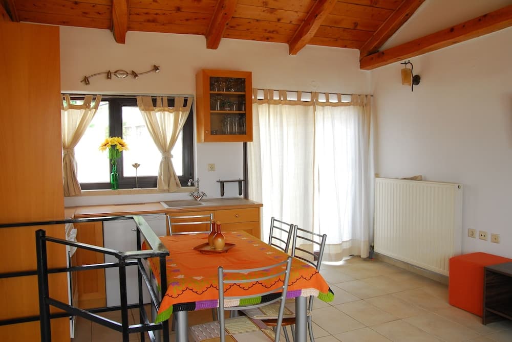 A cozy kitchen-dining area with wooden beams, an orange tablecloth, and large windows draped in white curtains, ideal for travelers seeking a warm and inviting rental space.