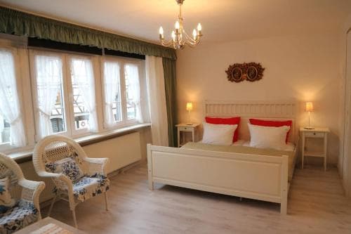 A cozy, warmly lit bedroom with a neatly made bed, vintage-style furniture, and large windows draped in green curtains, ideal for a relaxing getaway in a charming boutique hotel.