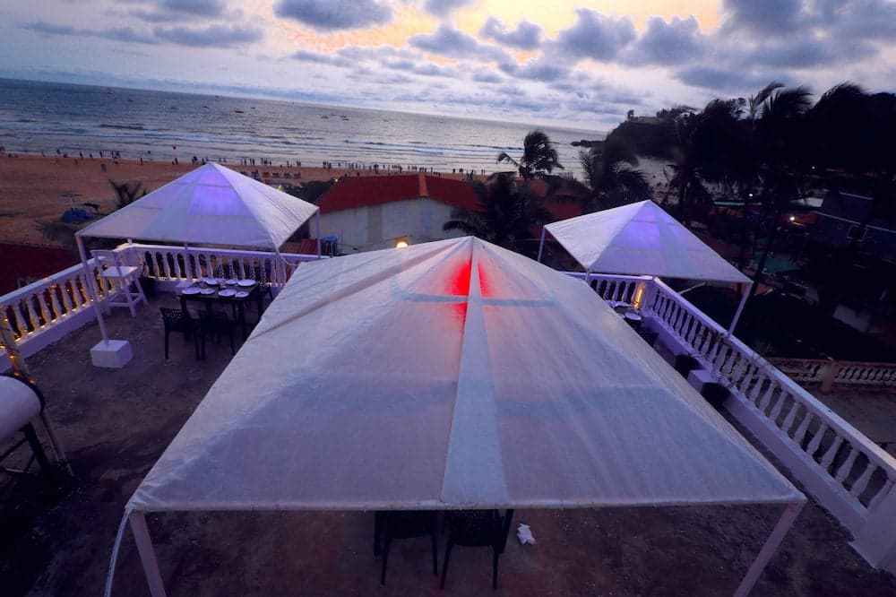 A serene beachside rooftop venue features white canopies and tables under a twilight sky, ideal for intimate gatherings or romantic dinners by the sea.