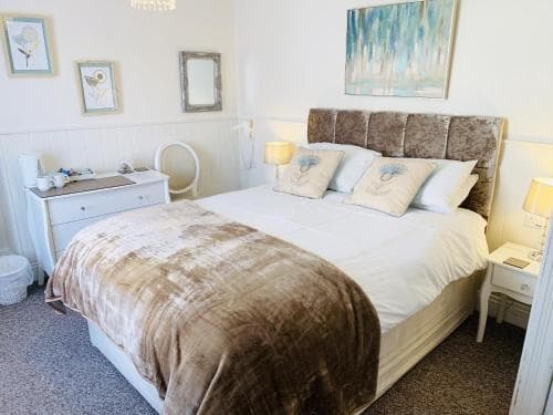 A cozy hotel room features a neatly made bed adorned with plush pillows and a brown throw blanket, framed by soft lighting and decorative wall art, creating a serene and inviting atmosphere ideal for travelers seeking relaxation.