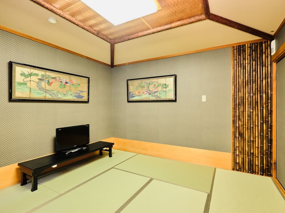 A serene Japanese-style room with tatami flooring, bamboo accents, framed artwork, and a small TV setup offers a tranquil atmosphere ideal for cultural immersion and relaxation during travel.
