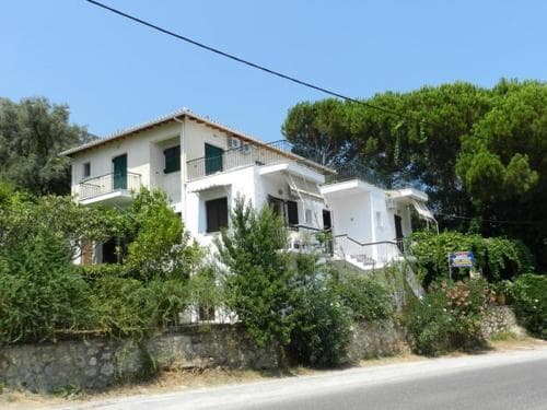 A serene two-story white villa surrounded by lush greenery under a clear blue sky offers an ideal retreat for travelers seeking a peaceful countryside getaway.