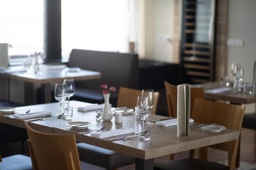 A cozy restaurant interior features neatly arranged tables with elegant glassware and floral accents, inviting travelers to enjoy a sophisticated dining experience in a modern setting.