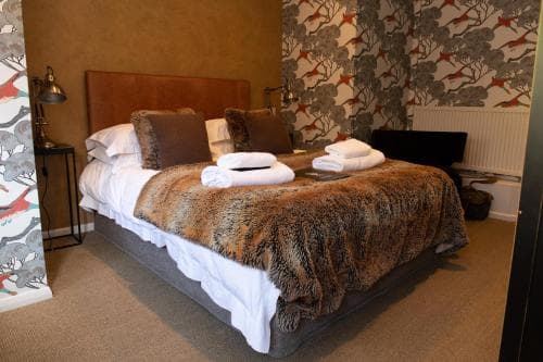 A cozy hotel room features a neatly made bed with plush bedding, patterned wallpaper, and warm lighting, ideal for travelers seeking comfort and relaxation.