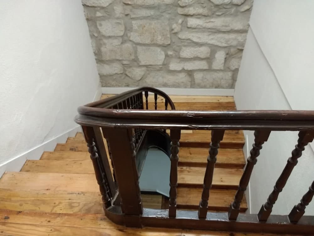 A rustic wooden staircase with a dark wooden railing ascends alongside a textured stone wall, creating an inviting atmosphere for travelers exploring historic interiors.