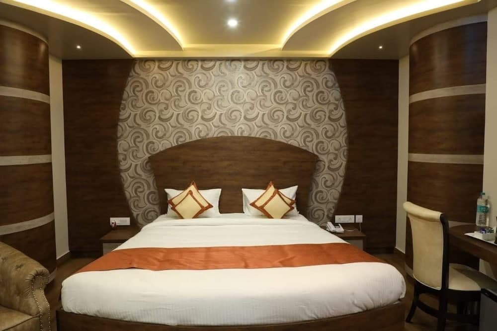A cozy hotel room features a neatly made bed with orange accents against a swirling patterned wall, complemented by warm lighting and wooden decor, ideal for travelers seeking comfort and relaxation.