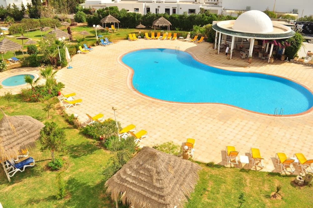 A vibrant resort pool area surrounded by lush greenery, thatched umbrellas, and colorful lounge chairs, exuding a relaxing tropical atmosphere ideal for vacationers seeking leisure and sunbathing spots.