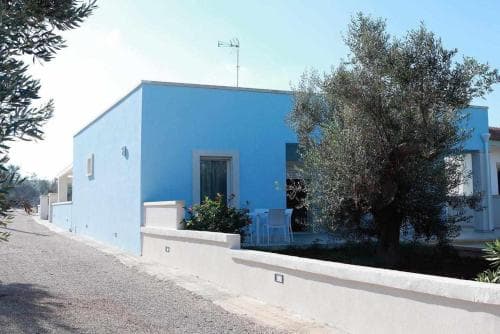 A serene Mediterranean villa with vibrant blue walls, lush greenery, and white accents invites travelers seeking a peaceful retreat in a picturesque coastal setting.