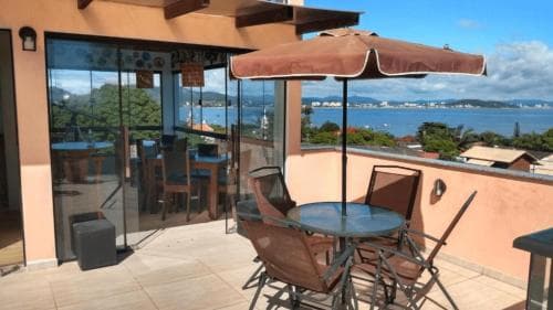 A serene balcony with a glass table, chairs, and an umbrella overlooks a picturesque bay, ideal for travelers seeking a tranquil seaside retreat.
