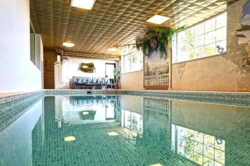 A serene indoor pool area with reflective water, tiled walls, and natural light streaming through large windows creates a tranquil spa-like atmosphere ideal for relaxation and wellness retreats.