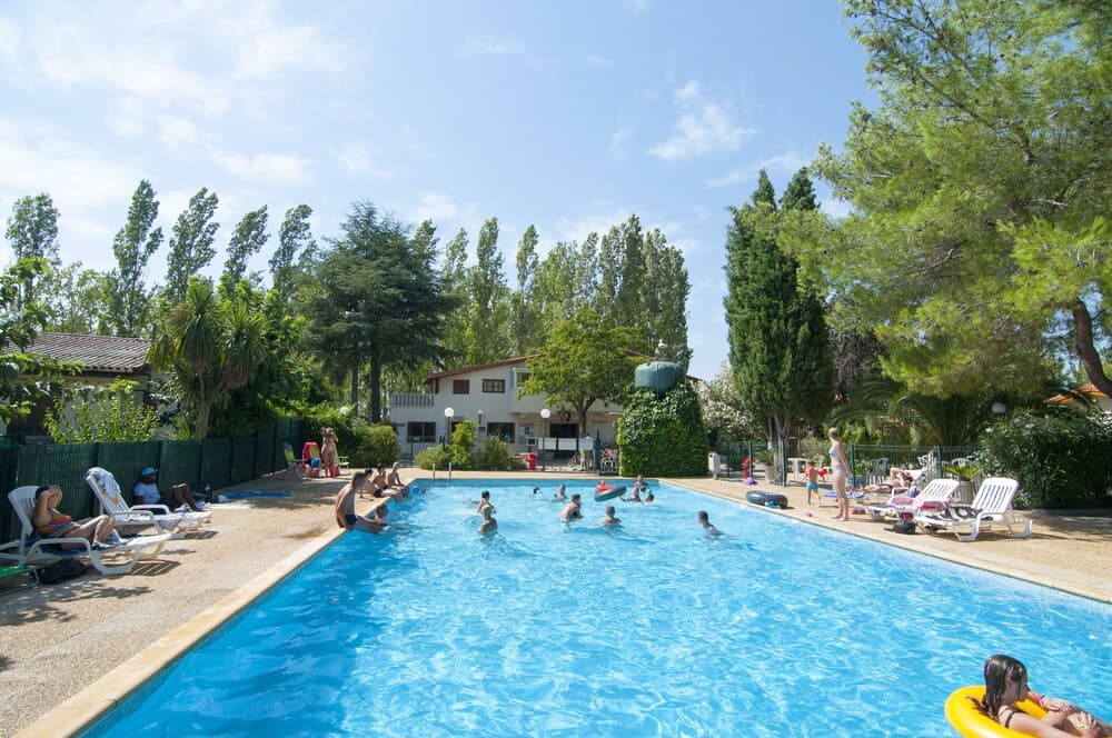 A vibrant outdoor swimming pool surrounded by lush greenery and lounge chairs offers a relaxing summer retreat for families seeking leisure and fun under the sunny sky.