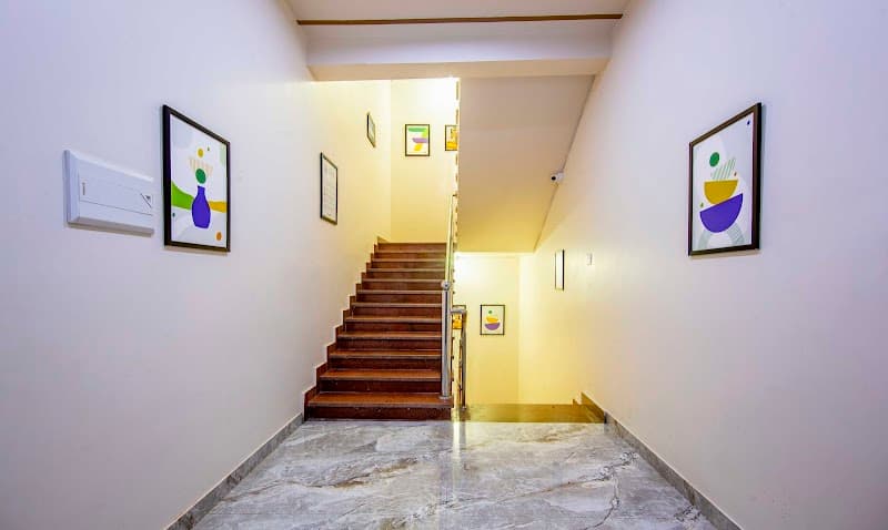 A warmly lit hotel corridor with marble flooring, wooden stairs, and colorful abstract art frames creates an inviting atmosphere ideal for travelers seeking comfort in Ayodhya, India.