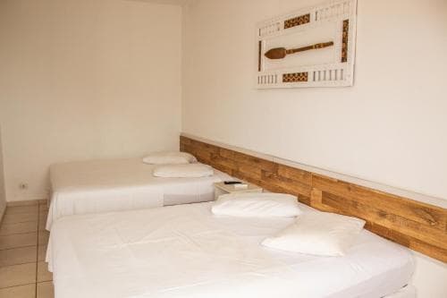 A cozy hotel room features two neatly made beds with white linens, a wooden headboard, and a decorative wall art piece, ideal for travelers seeking a simple and comfortable stay.