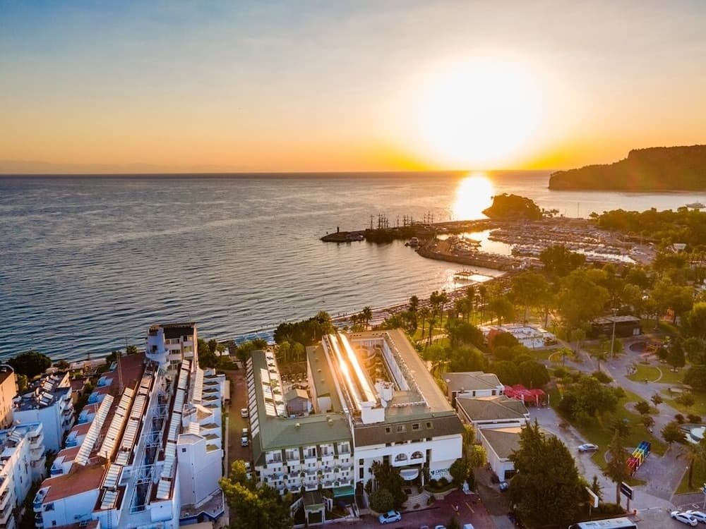 A serene coastal town at sunset showcases a picturesque marina, lush greenery, and modern buildings, ideal for travelers seeking a tranquil seaside retreat.