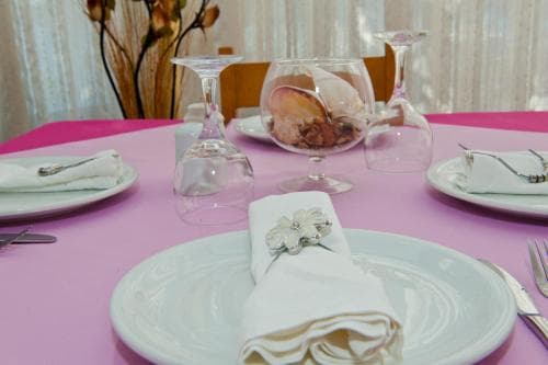 A beautifully set dining table with a pink tablecloth, white plates, elegant glassware, and decorative napkin rings creates an inviting atmosphere for a romantic dinner or special event.