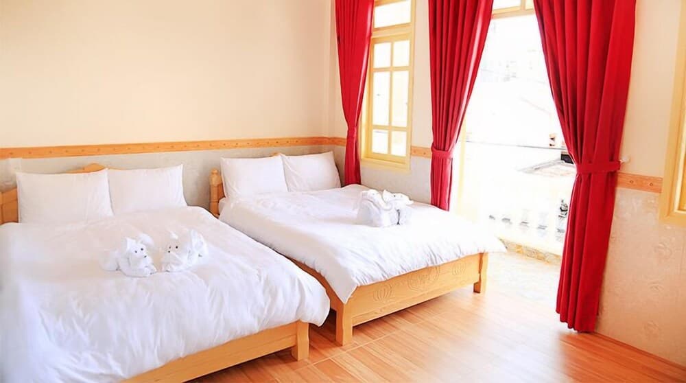 A cozy hotel room features two neatly made wooden beds adorned with towel animals, red curtains framing a bright window, and a warm, inviting atmosphere perfect for travelers seeking comfort and relaxation.