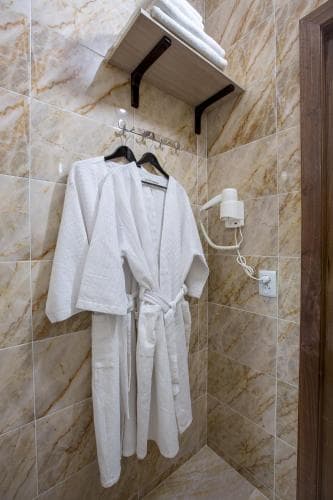 A cozy hotel bathroom features plush white robes hanging on hooks against marble-tiled walls, creating a serene and inviting atmosphere ideal for travelers seeking relaxation.