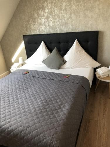 A cozy hotel room features a neatly made bed with gray bedding against a textured wall, creating a serene atmosphere ideal for travelers seeking relaxation.