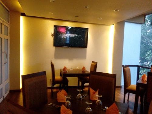 A cozy indoor dining area with warmly lit walls, modern furniture, and a mounted TV creates an inviting atmosphere perfect for travelers seeking a comfortable meal spot.