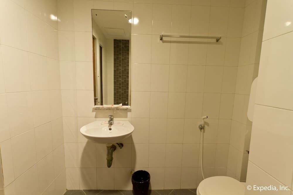 A clean, compact bathroom with white tiled walls, a sink, mirror, toilet, and handheld showerhead offers a functional space ideal for travelers seeking basic amenities in a hotel or guesthouse.