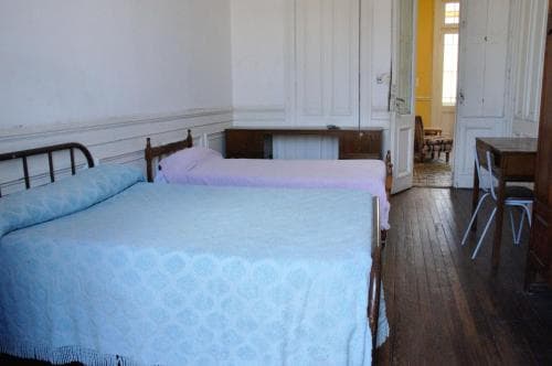 A cozy, rustic bedroom with twin beds draped in pastel linens invites travelers seeking a quaint and peaceful retreat in a vintage-style accommodation.
