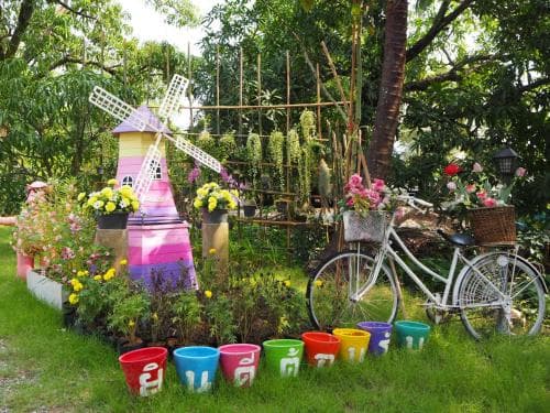 A vibrant garden scene featuring a colorful windmill, a bicycle adorned with flowers, and assorted planters, evokes a cheerful and whimsical atmosphere ideal for family-friendly outdoor exploration.