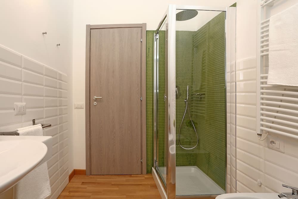 A modern bathroom with white tiled walls, a green mosaic shower enclosure, wooden flooring, and a sleek sink setup creates a clean and inviting atmosphere ideal for travelers seeking comfort and style in their accommodations.