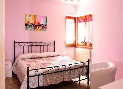 A cozy bedroom with pink walls, a metal bed frame, and a window with curtains offers a serene retreat, ideal for travelers seeking a charming and comfortable accommodation.