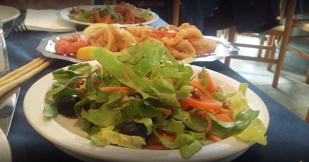 A vibrant salad with fresh greens, olives, and carrots sits invitingly on a restaurant table alongside crispy fried calamari, perfect for travelers seeking a delightful Mediterranean dining experience.