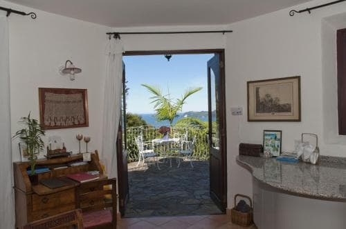 A cozy indoor space opens to a serene outdoor patio with sea views, ideal for a tranquil vacation retreat, featuring framed artwork, a wooden desk, and lush greenery enhancing the peaceful ambiance.