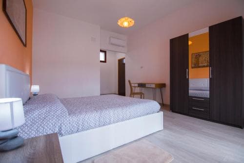 A cozy bedroom with soft lighting, wooden furniture, and a neatly made bed creates a serene atmosphere ideal for travelers seeking relaxation in a modern apartment setting.