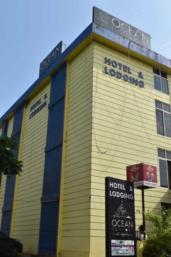 A vibrant yellow and blue hotel named "Ocean Comfort" stands invitingly under a clear sky, featuring bold signage and lush greenery, ideal for travelers seeking coastal accommodations.