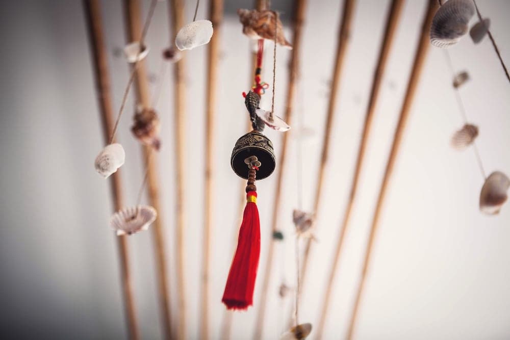 A serene indoor setting features bamboo sticks adorned with seashells and a central bell with a red tassel, creating a calming atmosphere ideal for meditation or relaxation spaces.