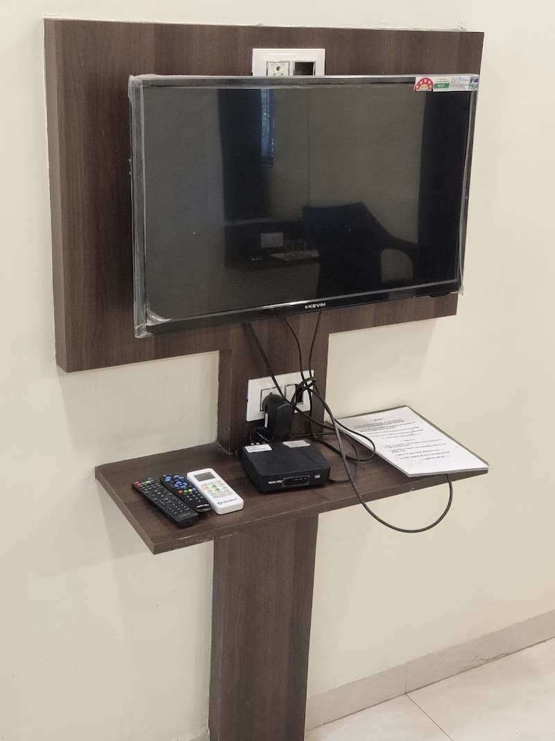A cozy living space setup featuring a mounted TV with remote controls on a wooden shelf, ideal for travelers seeking comfort near the bus stand in Takve Kurth, Pune, India.