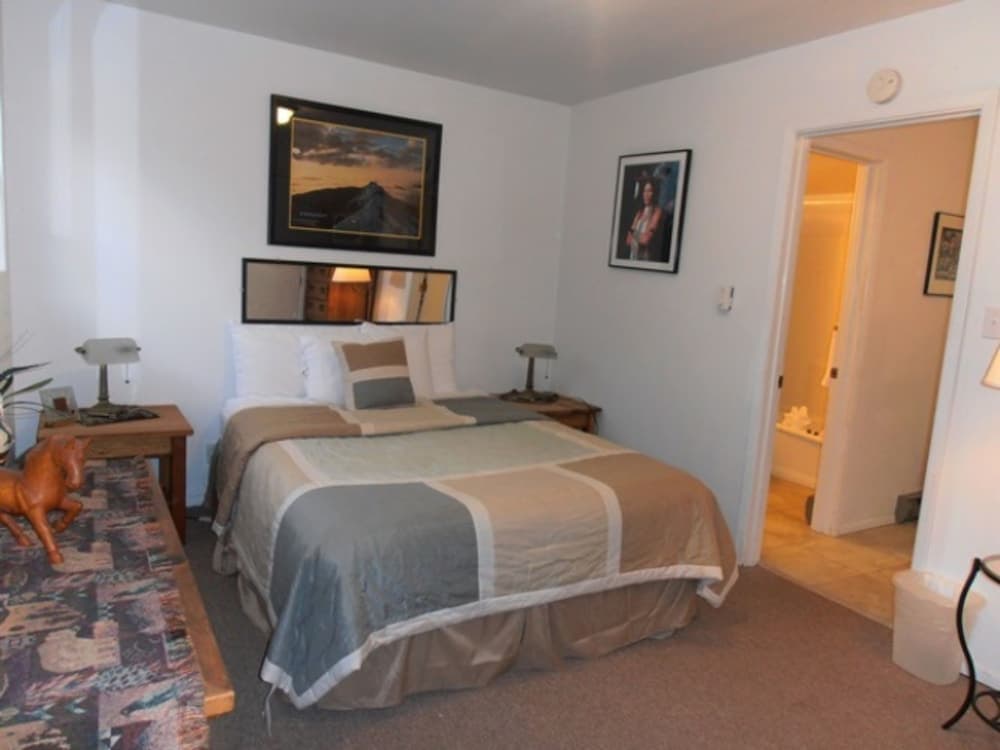 A cozy hotel bedroom features a neatly made bed with neutral linens, framed artwork on the walls, and a view into an adjacent bathroom, ideal for travelers seeking comfort and convenience.