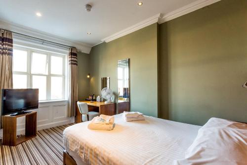 A cozy hotel room with soft green walls, a neatly made bed, a wooden desk by the window, and a modern TV setup, ideal for travelers seeking comfort and relaxation.