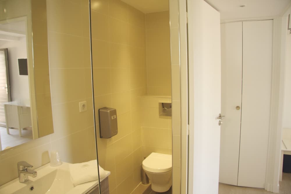 A modern bathroom with beige tiles, a sleek sink, a toilet enclosed in glass, and a mirrored vanity exudes a clean and functional ambiance ideal for travelers seeking comfort and convenience.