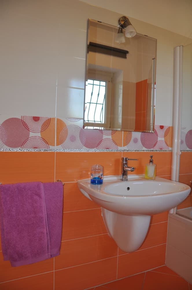 A cozy bathroom with orange tiles, a vibrant patterned border, and a purple towel creates a cheerful ambiance, ideal for travelers seeking a bright and inviting accommodation space.