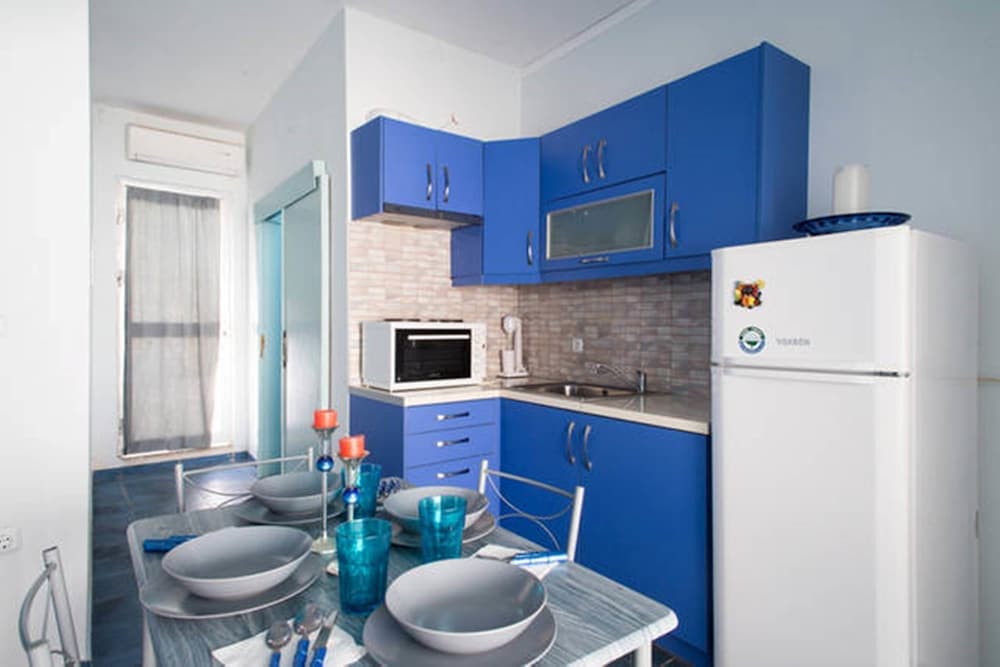 A cozy apartment kitchen with vibrant blue cabinets, a white refrigerator, and a dining table set for four, ideal for travelers seeking a homey and functional space for self-catering stays.