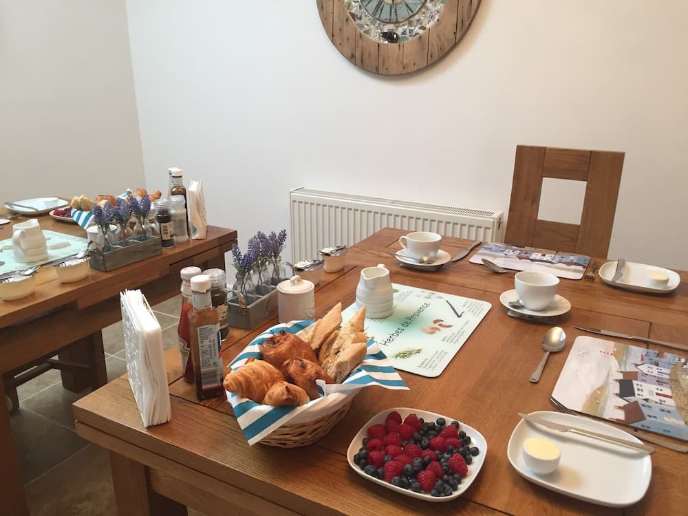 A cozy dining room setup with a wooden table adorned with fresh pastries, berries, and coffee cups, evokes a welcoming breakfast atmosphere ideal for travelers seeking a comfortable and inviting start to their day.