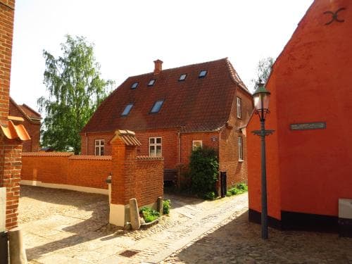 A charming cobblestone courtyard surrounded by red-brick buildings under a bright sky evokes a peaceful European village atmosphere, ideal for travelers seeking historic architecture and serene exploration.