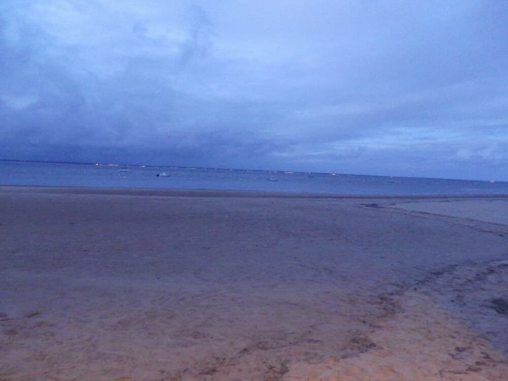 A serene beach at dusk features calm waters under a cloudy sky, ideal for tranquil evening walks and photography enthusiasts.