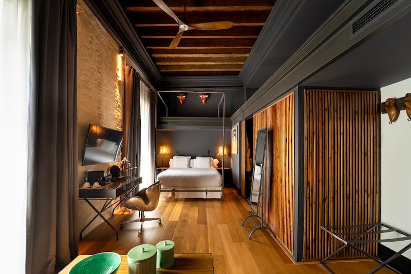 A cozy hotel room in Sevilla's historic Casco Antiguo features rustic brick walls, wooden floors, and modern furnishings, creating an inviting atmosphere perfect for travelers seeking comfort and charm.